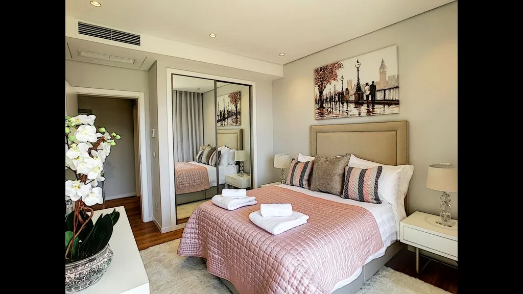 A bedroom with a bed dressed in a pink quilt and decorative pillows.
