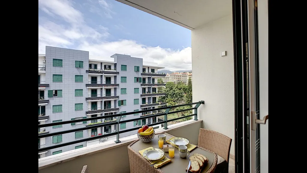 A balcony with a table and seating overlooks nearby apartment buildings.