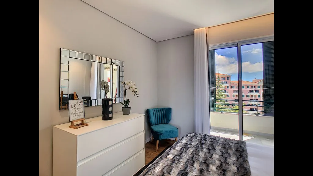 A bedroom with a bed, dresser, and a window overlooking nearby buildings.