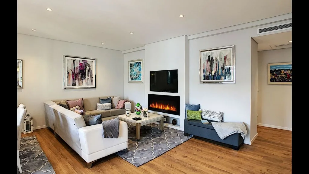 A bright living room with seating arranged around a fireplace and television.