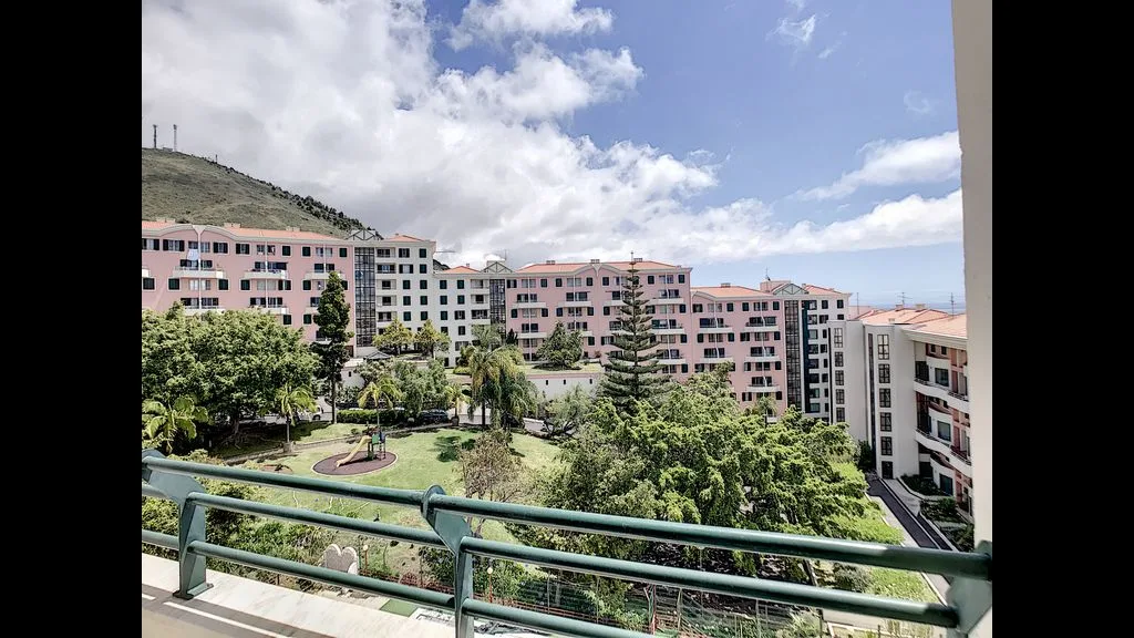 A balcony overlooks apartment buildings, trees, and a landscaped courtyard.