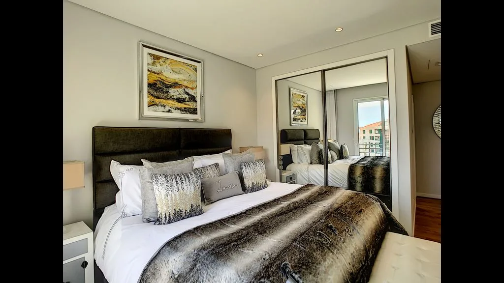A bedroom with a bed, decorative pillows, and mirrored closet doors.