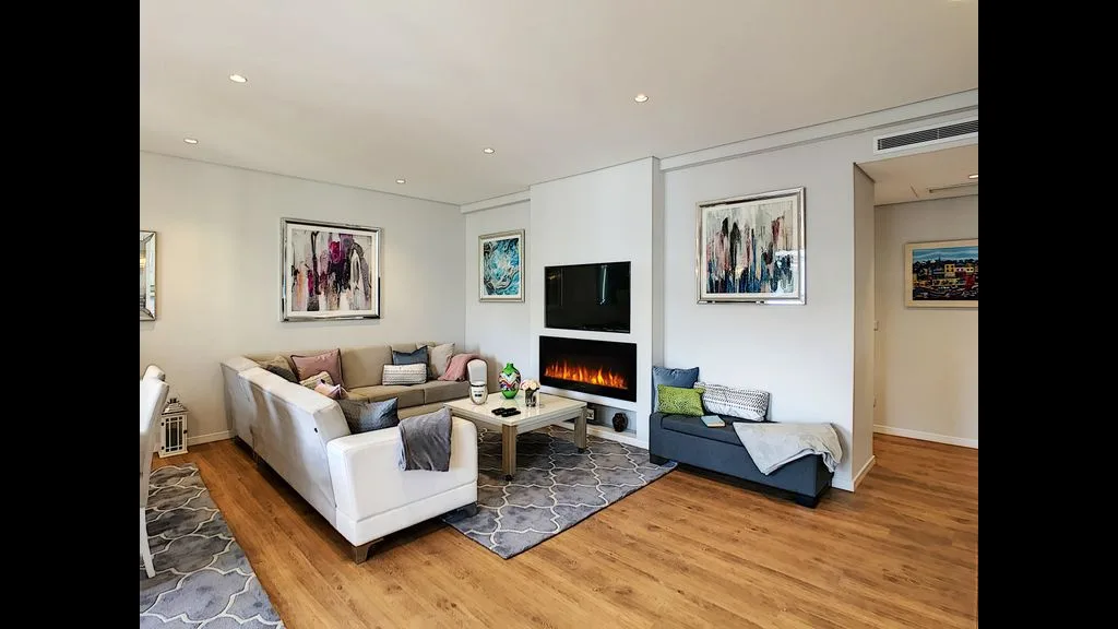 A bright living room with seating arranged around a fireplace and television.