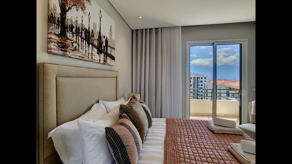 A bedroom with a neatly made bed beside a balcony door.