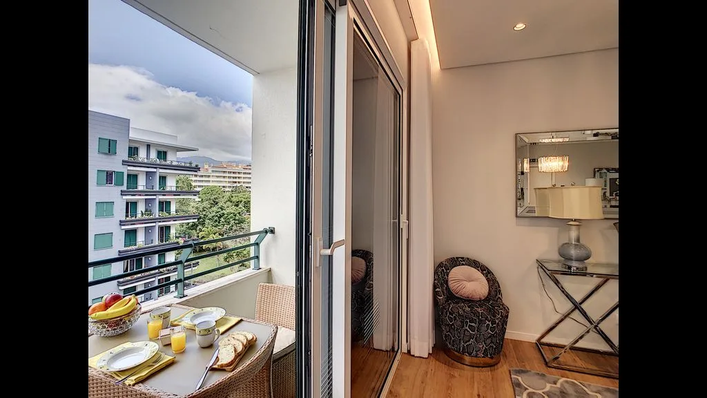 A bright dining area opens onto a balcony overlooking nearby buildings.