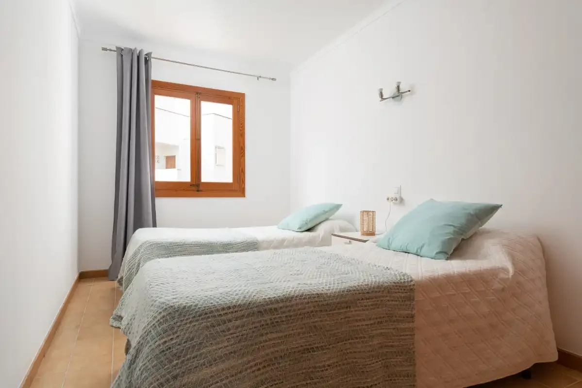 A bright bedroom with two beds and a wooden-framed window.