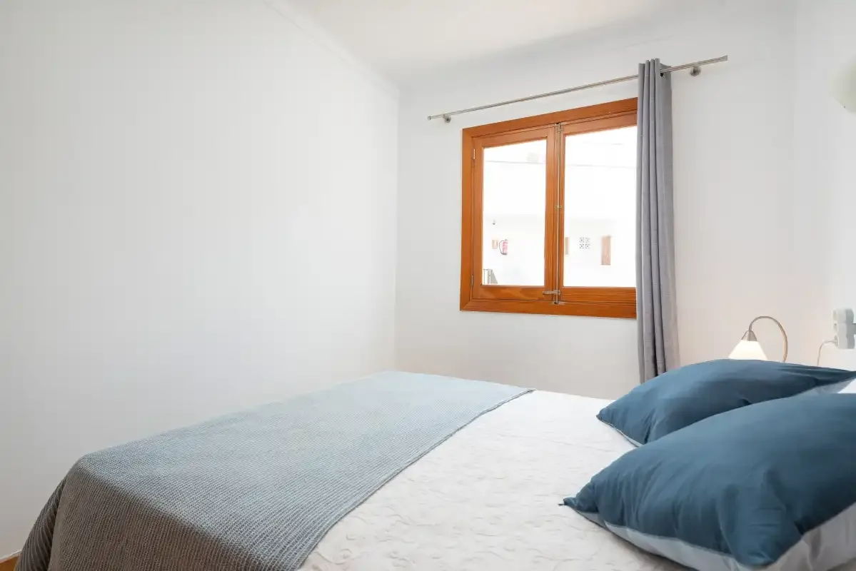 A bedroom with a bed beside a wooden-framed window.