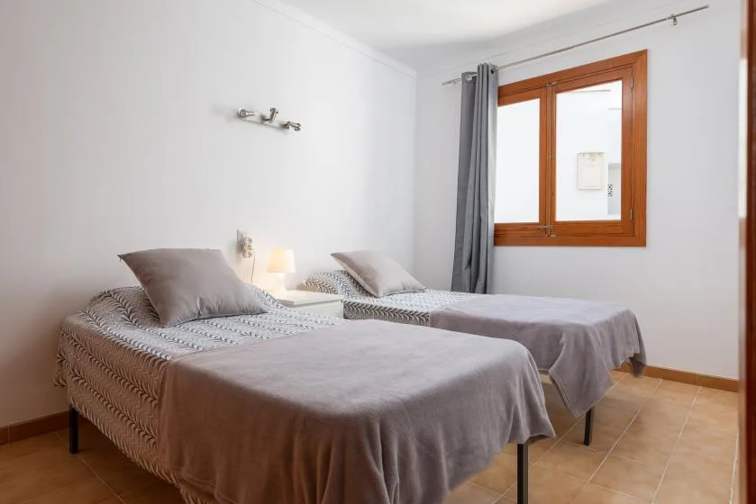 A twin bedroom with two beds and a window framed by gray curtains.