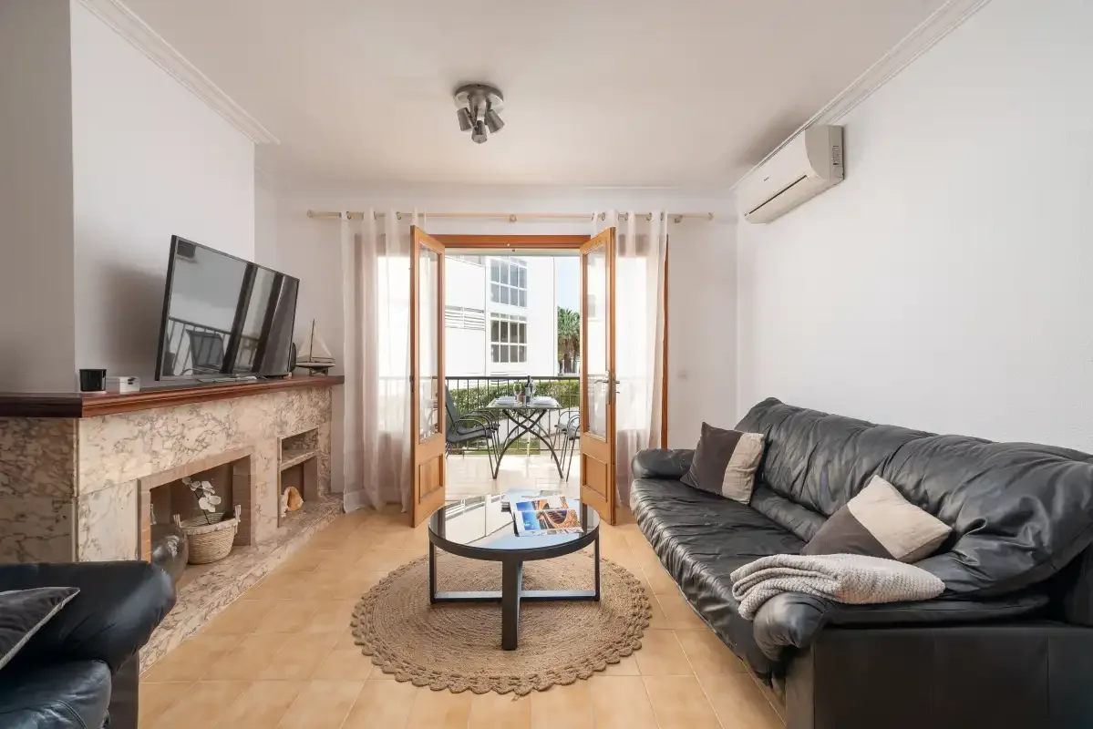 A living room with leather seating, a television, and open doors to a balcony.