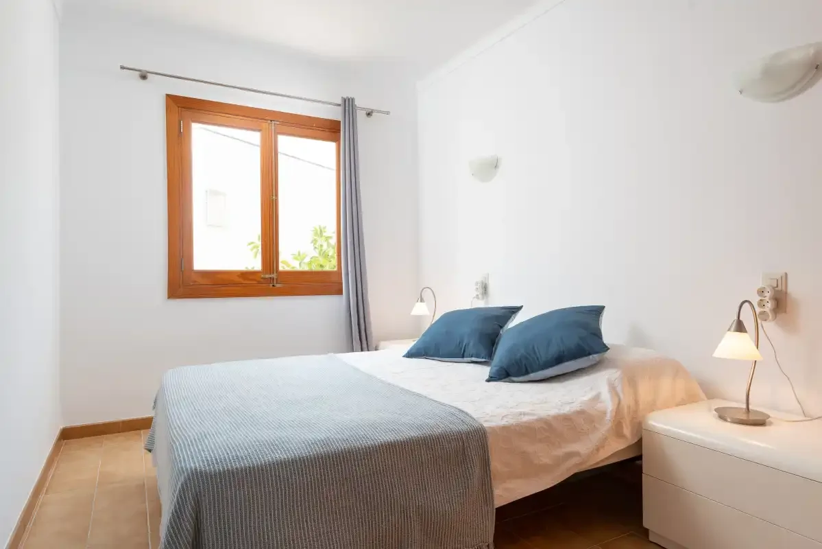 A bedroom with a bed dressed in white and blue bedding beside a window.