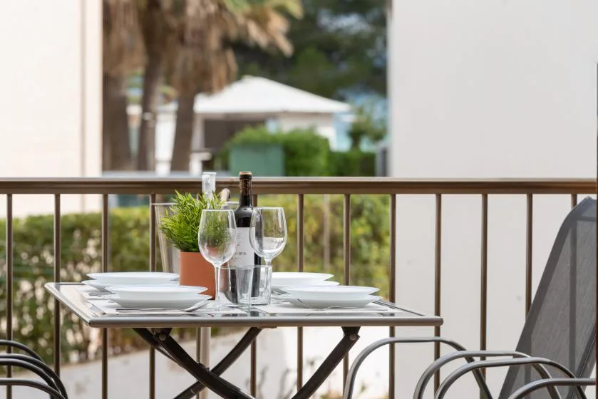 A small outdoor dining table is set with plates and glasses beside a balcony railing.
