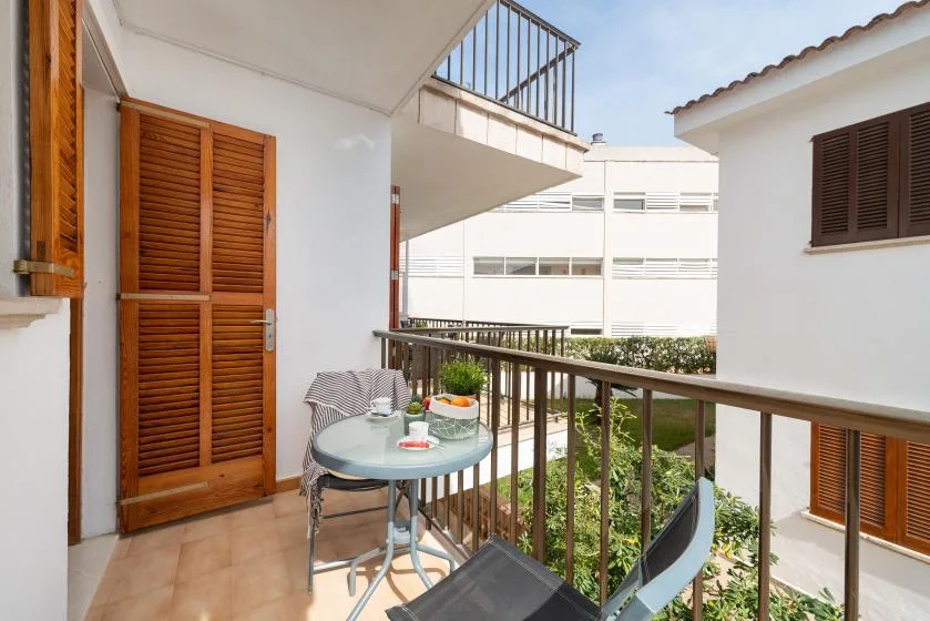 A small balcony with a glass table and seating overlooks neighboring buildings.
