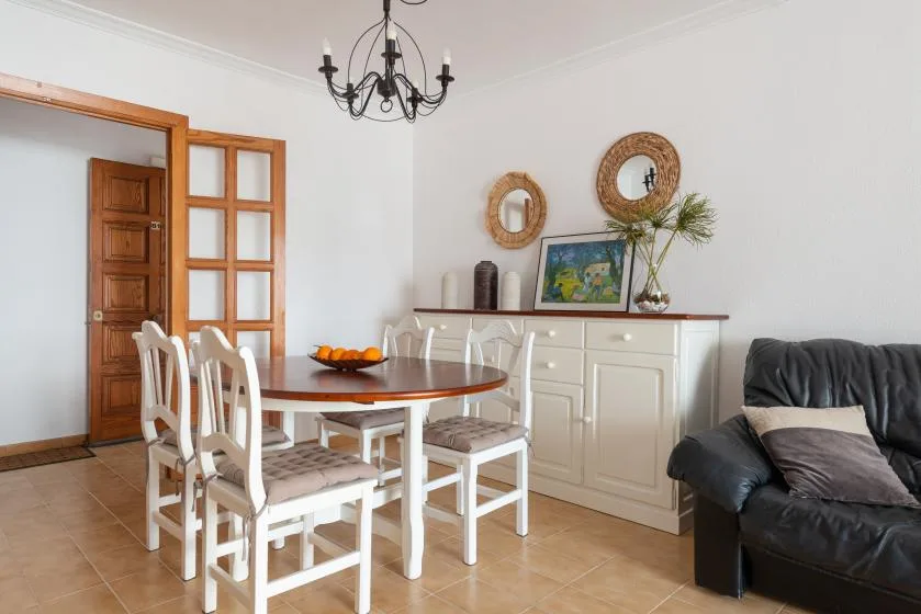 A dining area with a wooden table and white chairs beside a living room seating area.