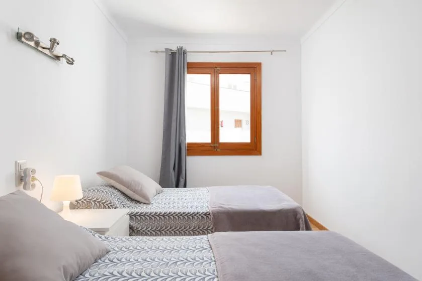 A bright bedroom with two beds and a window with gray curtains.