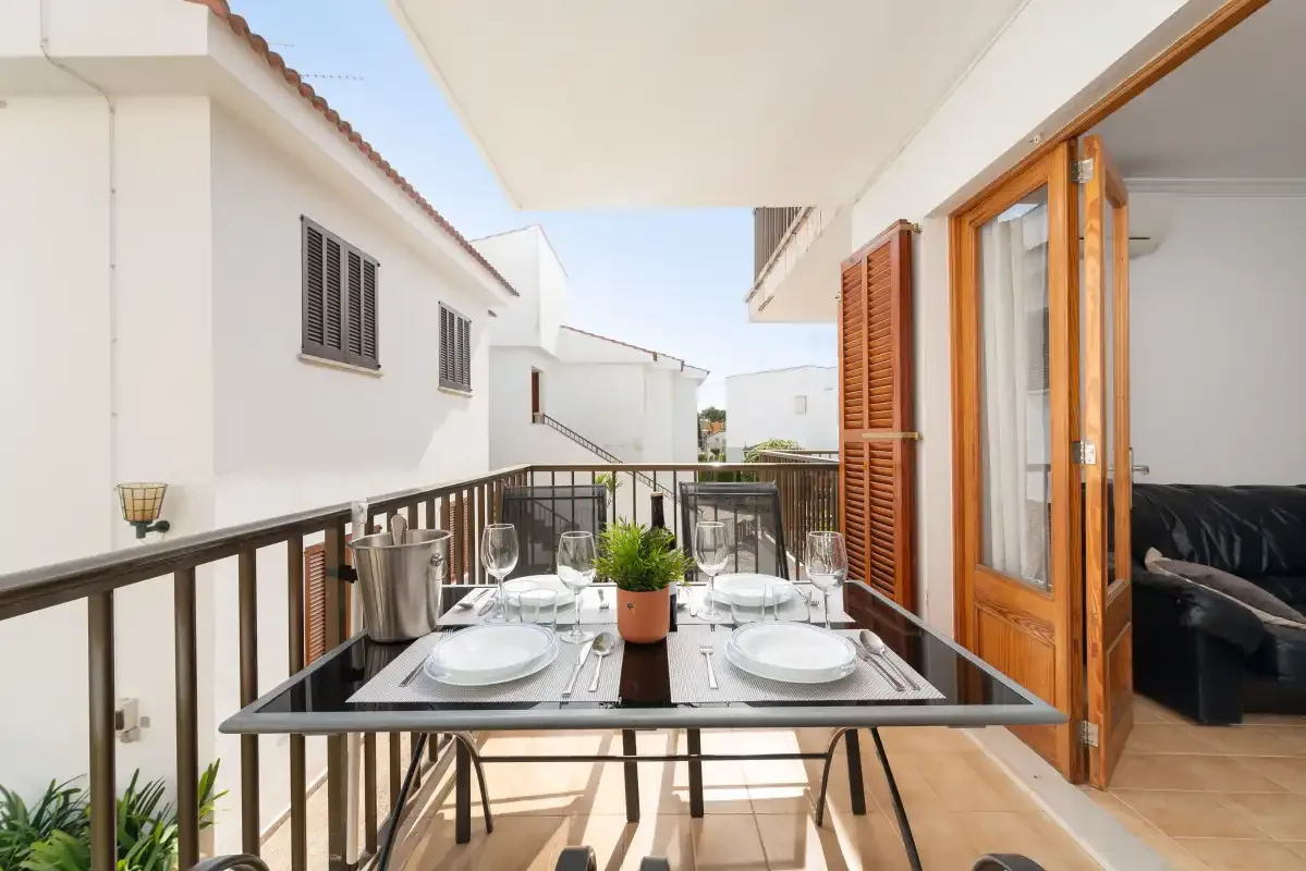 A balcony dining area has a set table beside open wooden doors.