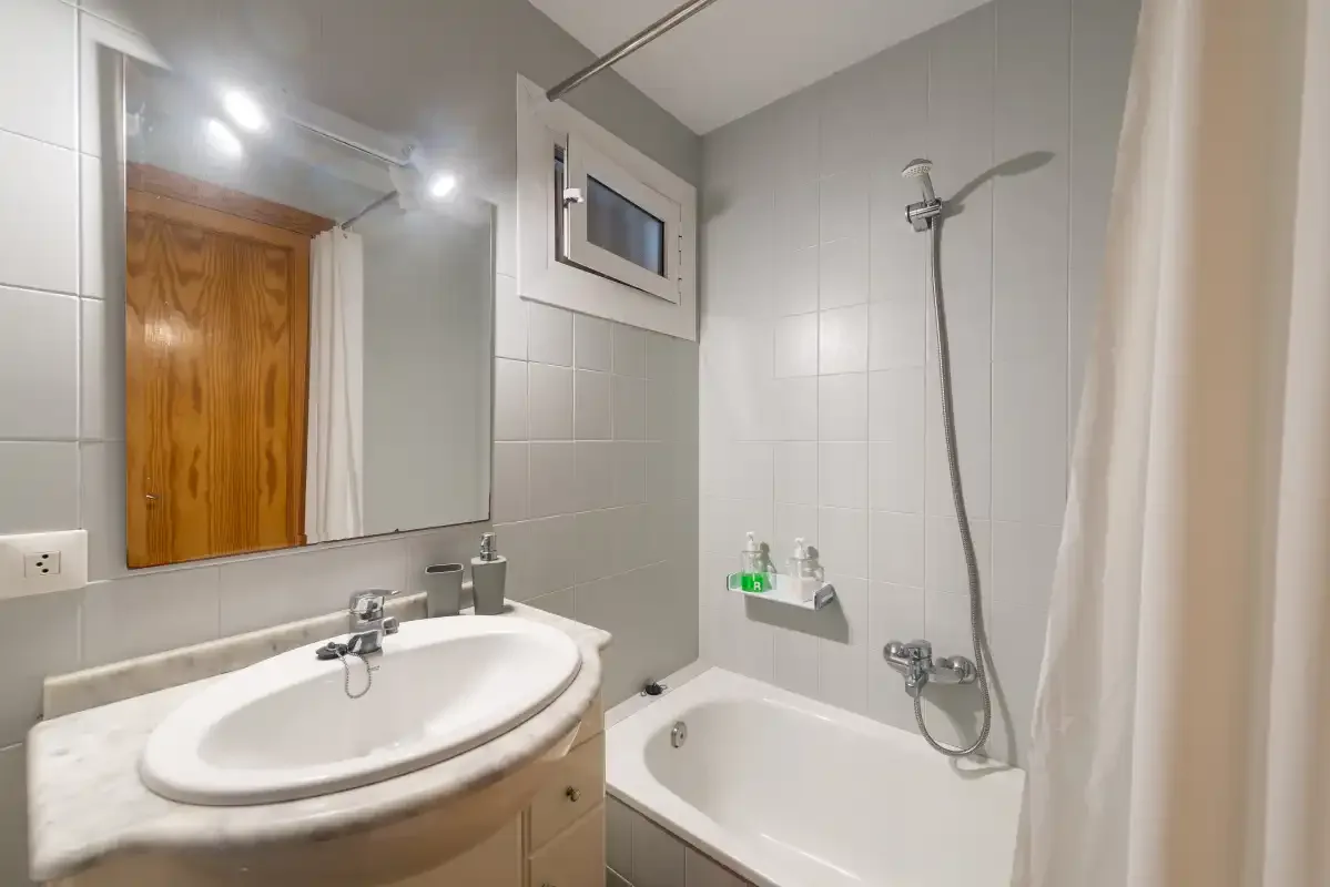 A tiled bathroom with a sink, mirror, and bathtub.