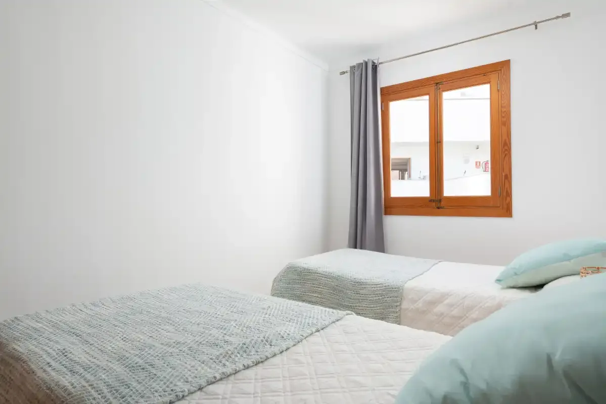 A bright bedroom with beds and a wooden-framed window.