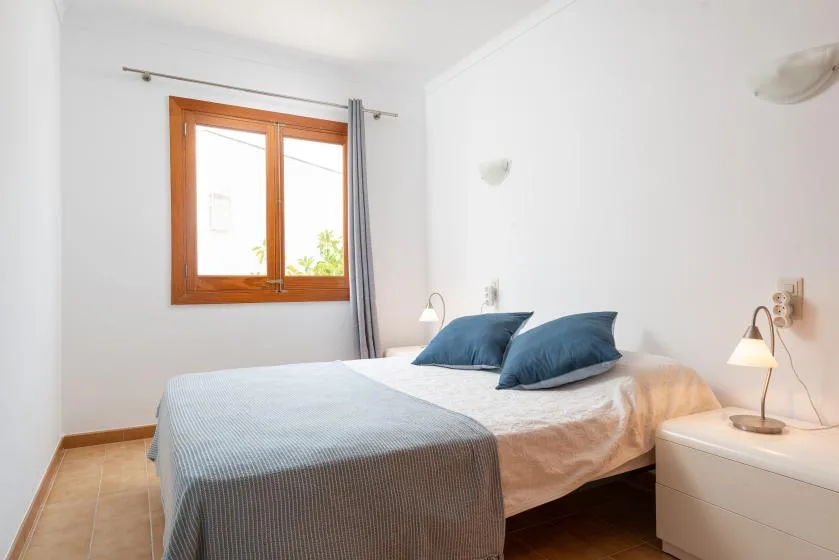 A bedroom with a bed, blue pillows, and a window with curtains.