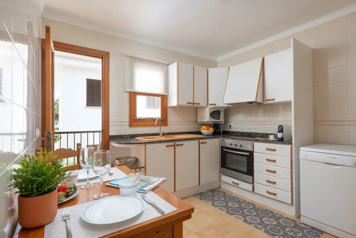 A bright kitchen with cabinets, a countertop, and a dining table set with dishes.