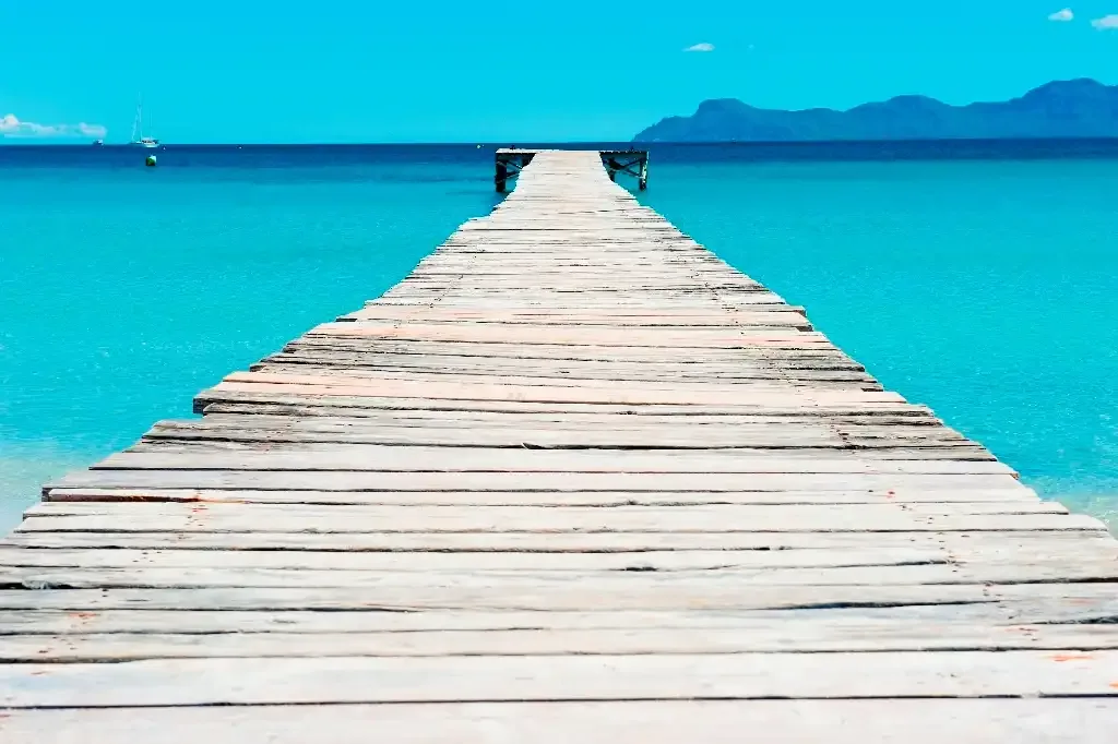 A wooden pier extends across bright turquoise water toward distant mountains.