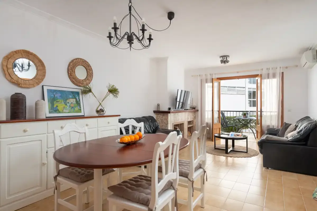 A dining and living room with a table, seating, and a balcony beyond.