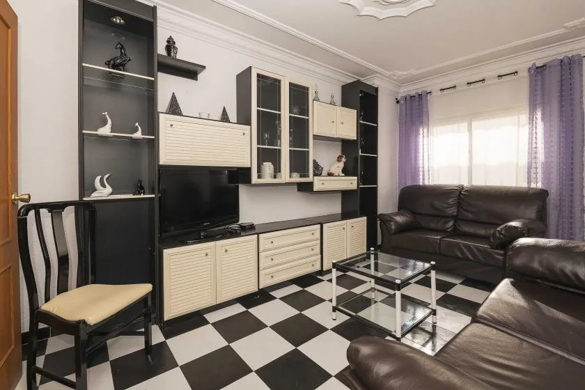 A living room with dark seating, a glass coffee table, and a black-and-white checkered floor.