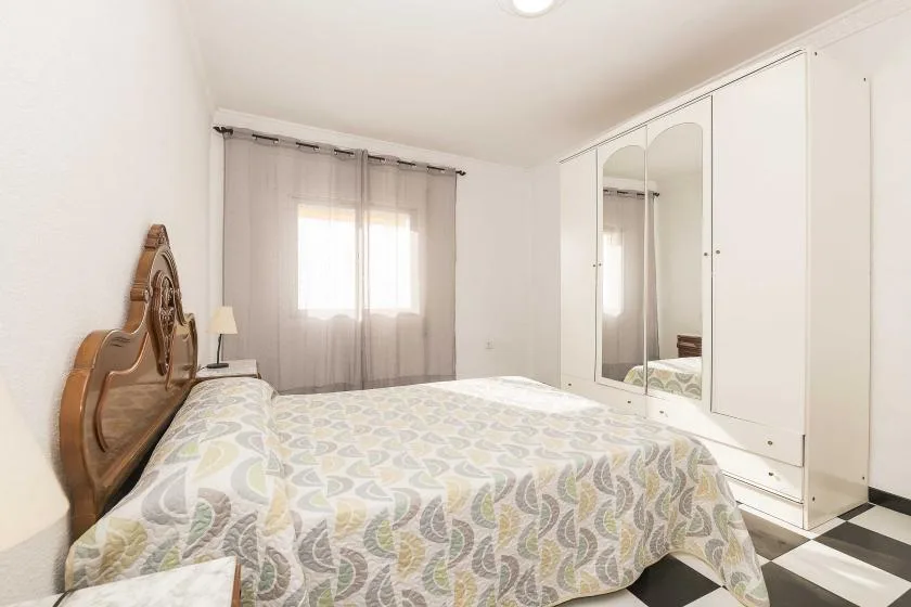 A bedroom with a patterned bedspread, a curtained window, and mirrored wardrobes.
