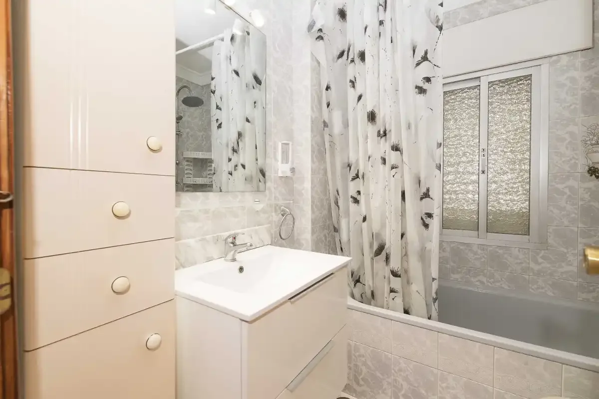 A bathroom with a sink, mirror, and bathtub behind a patterned curtain.