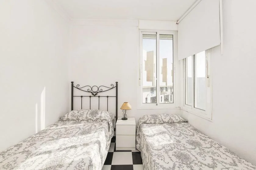 A bright bedroom with two beds beside large windows.