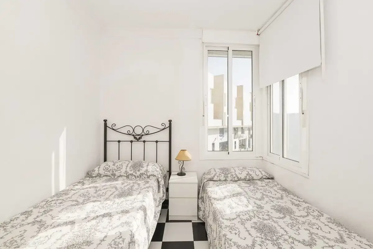 A bright bedroom with two single beds and windows along the wall.