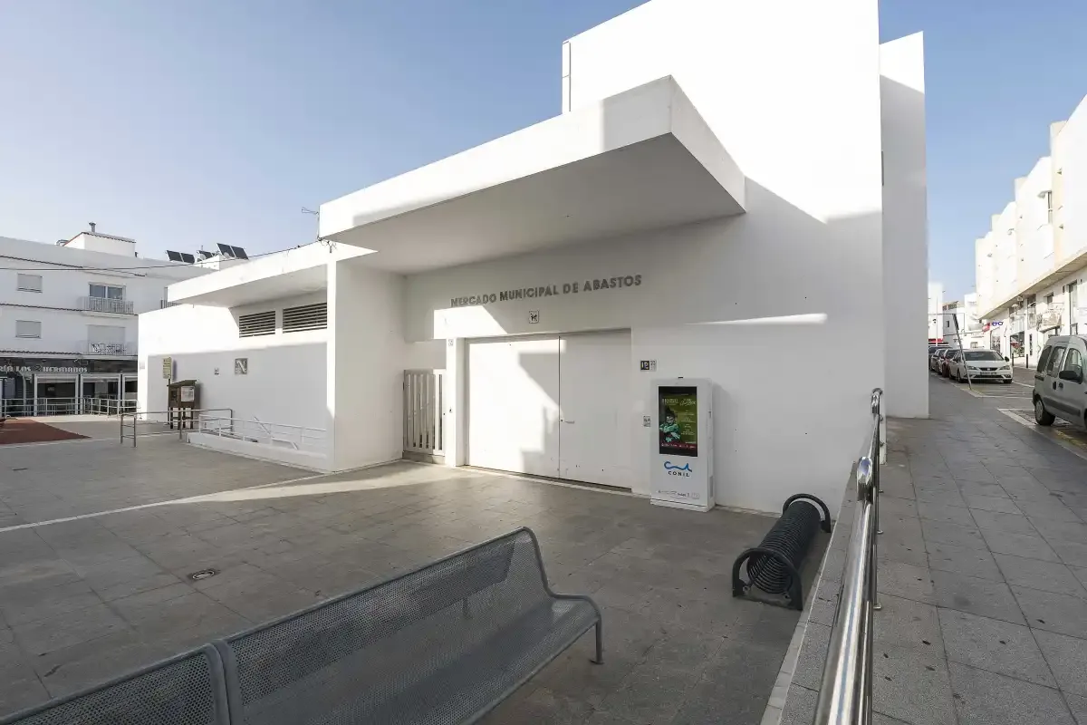 A white municipal building faces a paved public plaza with benches.