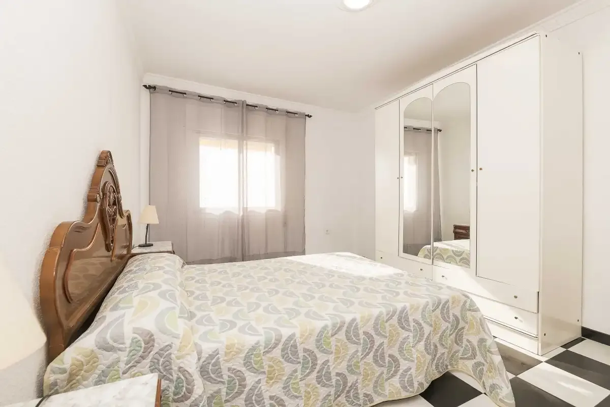 A bedroom with a bed, curtained window, and mirrored wardrobe.