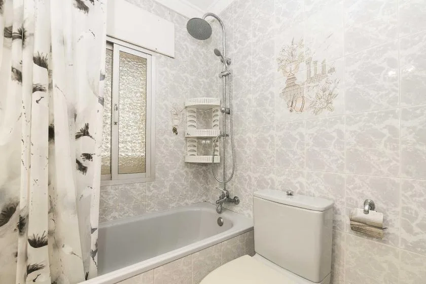A bathroom with a bathtub, shower, and toilet beside a window.