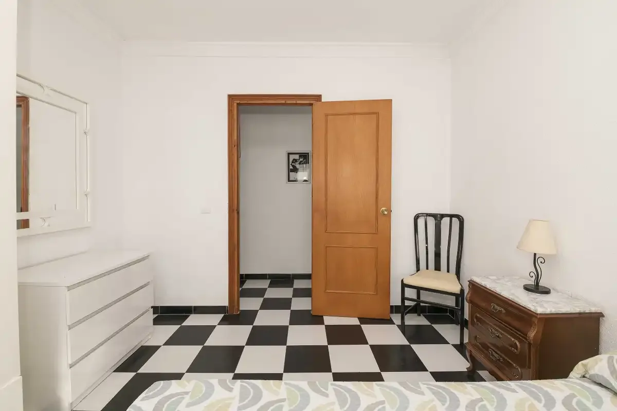 A bedroom with a black-and-white tiled floor and an open wooden door.