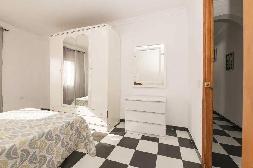 A bedroom with a bed, mirrored wardrobe, and dresser on a checkered floor.