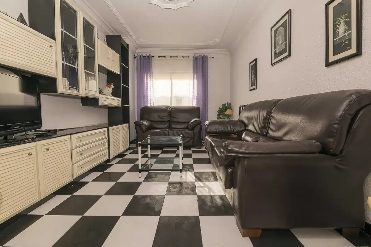 A living room with dark seating, a glass coffee table, and a checkerboard floor.