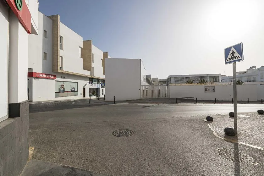 A paved street-side area beside white commercial buildings, with a pedestrian crossing sign.
