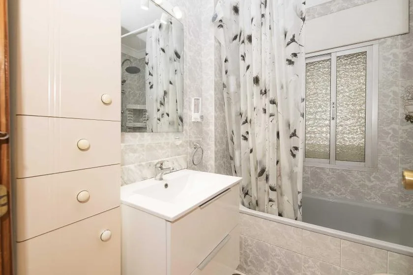 A tiled bathroom with a sink, mirror, bathtub, and patterned shower curtain.