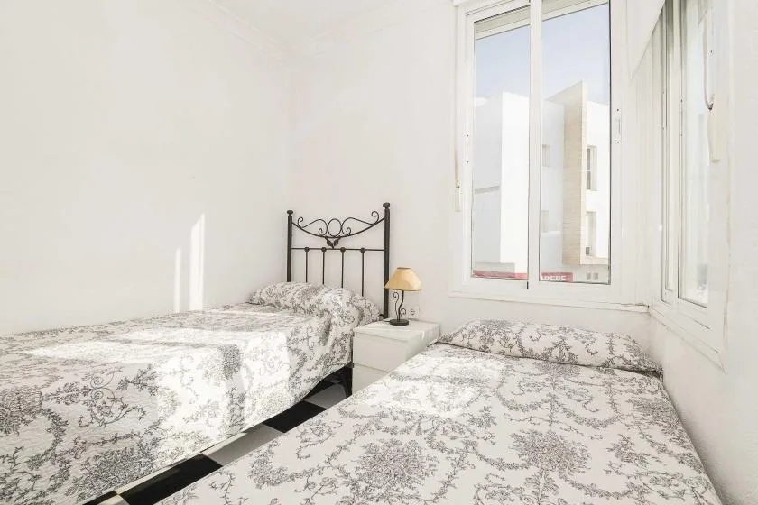 A bright bedroom with two beds beside large windows.