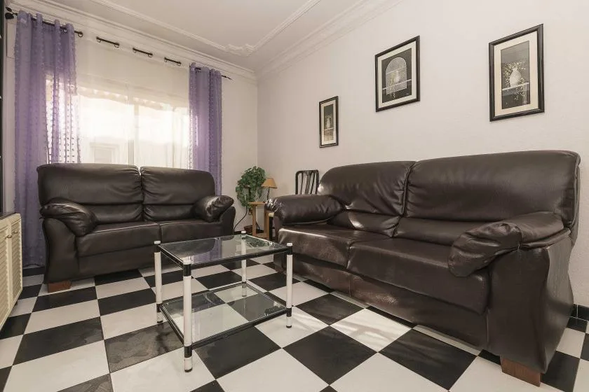 A living room with dark seating, a glass coffee table, and a checkered floor.