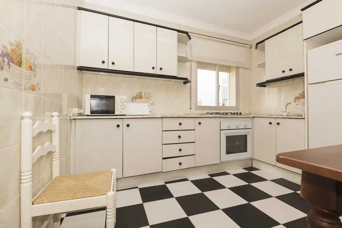 A bright kitchen with white cabinets, a countertop oven, and a black-and-white checkered floor.