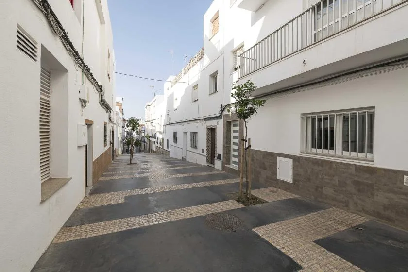 A narrow paved street runs between white buildings with barred windows.