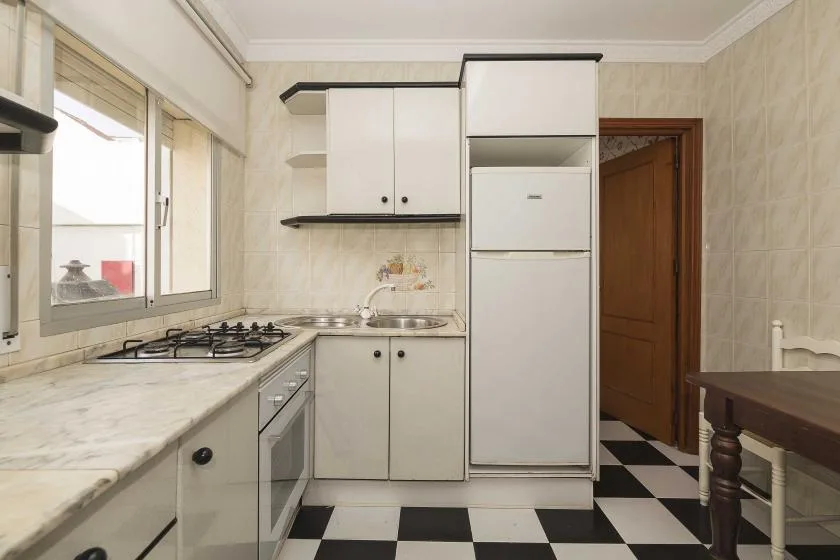 A galley kitchen with white cabinets, a countertop, and a black-and-white checkered floor.