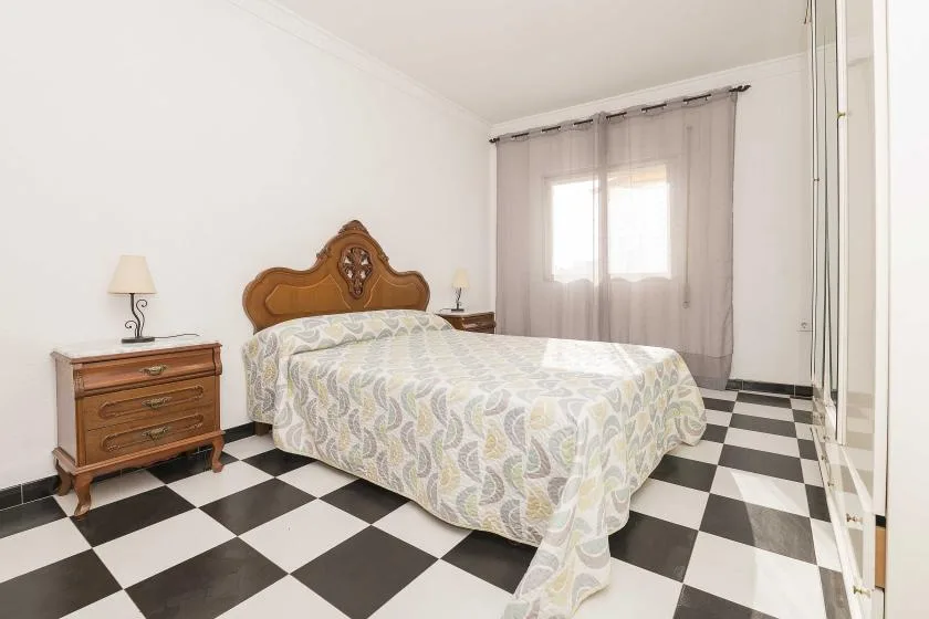 A bedroom with a patterned bedspread, wooden headboard, and checkered floor.