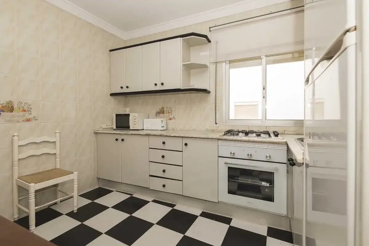 A bright kitchen with white cabinets and a black-and-white checkerboard floor.