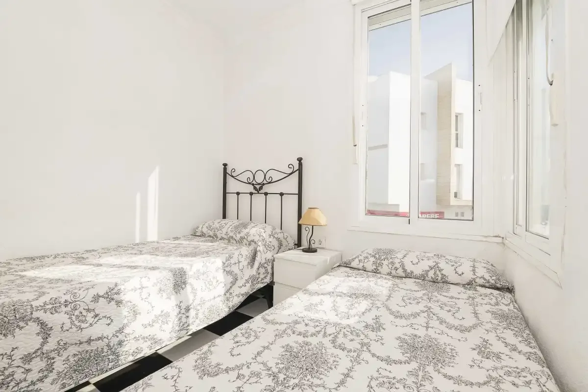 A bright bedroom with two beds covered in matching patterned bedding.