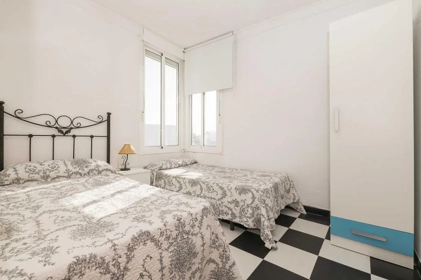A bright bedroom with patterned bedding, windows, and a black-and-white tiled floor.
