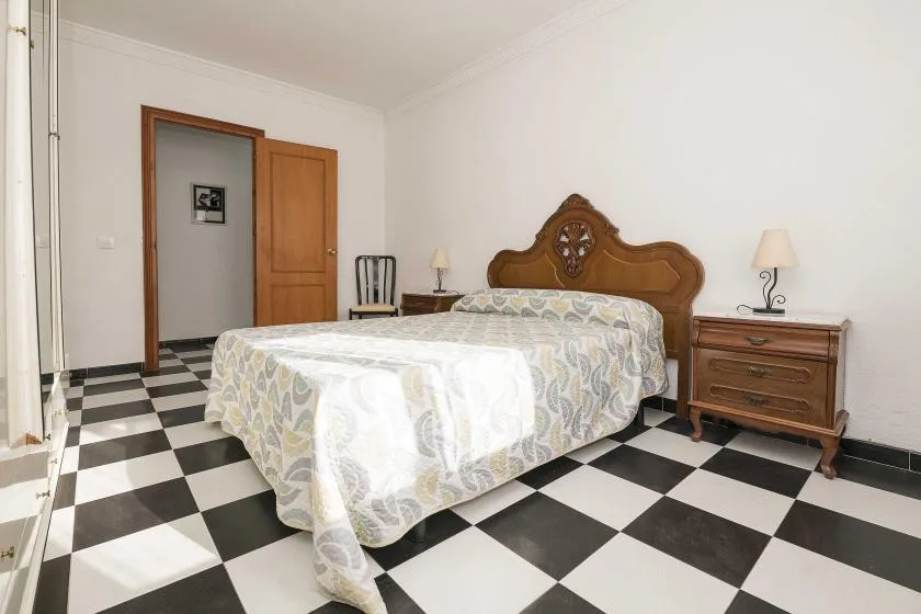 A bedroom with a patterned bedspread, wooden headboard, and checkerboard floor.