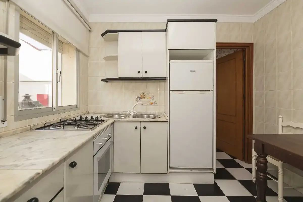 A bright kitchen with white cabinets, a countertop, and a black-and-white tiled floor.