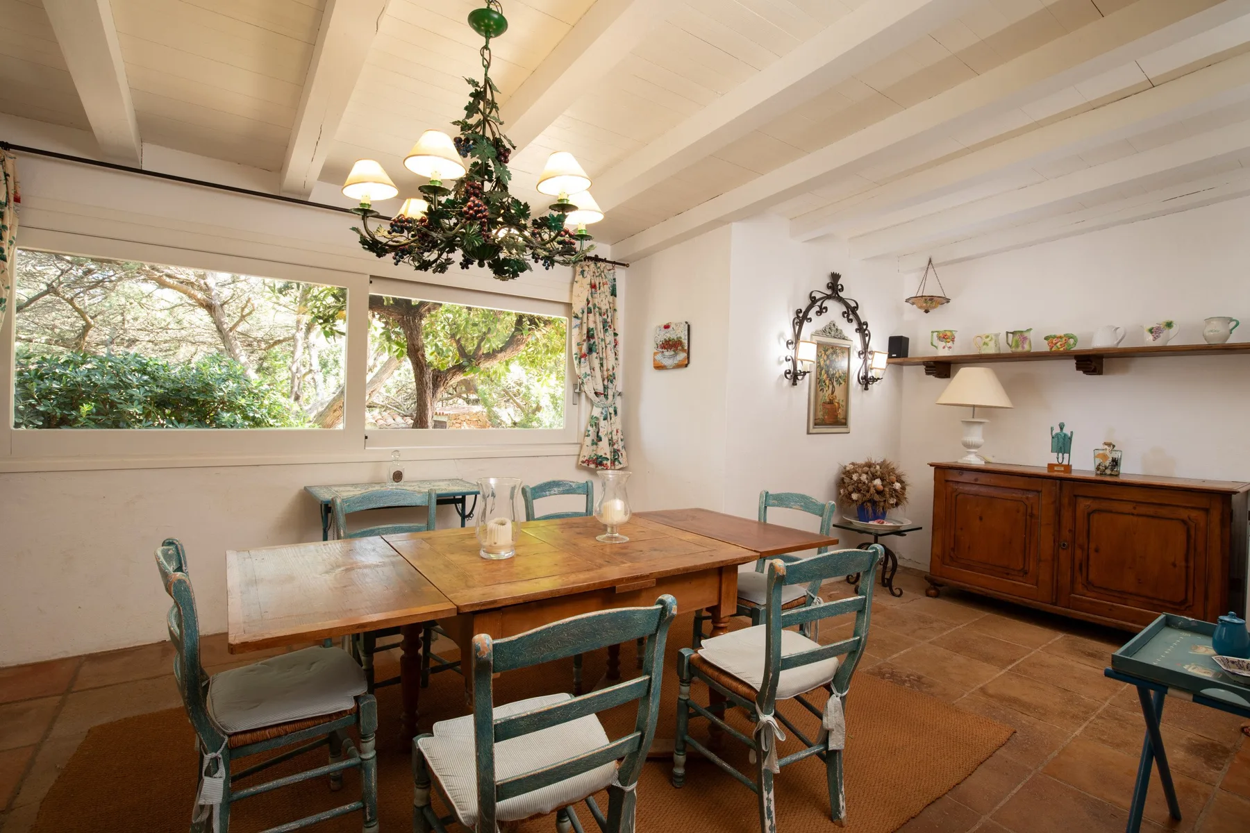A dining room with a wooden table, chairs, and windows overlooking trees.